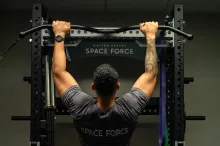 Man doing a pull-up on a bar in a gym, wearing a Space Force t-shirt.